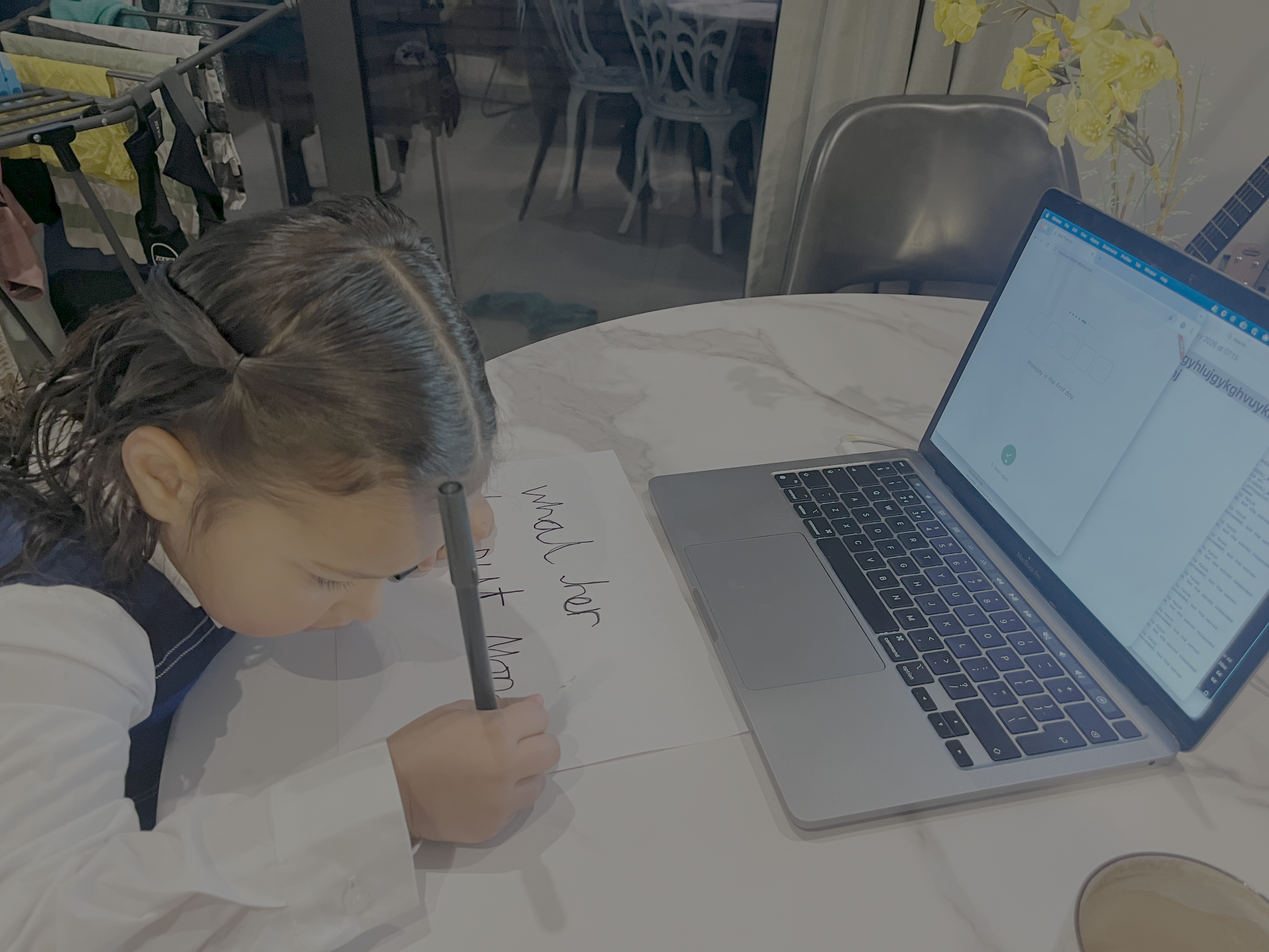 Handwritten spelling words on paper beside a laptop showing the app's photo upload screen.